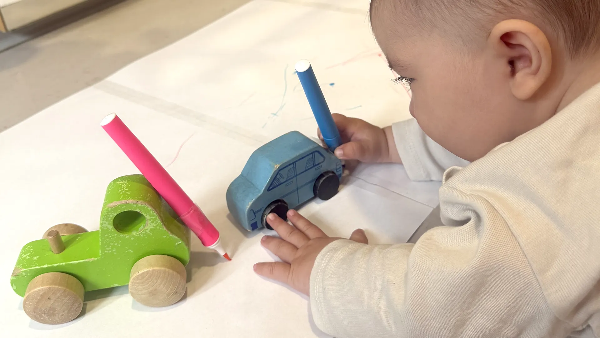 Un enfant à la crèche La Nanosphère à Lausanne dessine avec une voiture équipée d’un feutre sur une grande feuille au sol.
