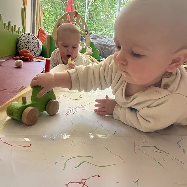 Un enfant à la crèche La Nanosphère à Lausanne dessine avec une voiture équipée d’un feutre sur une grande feuille au sol.