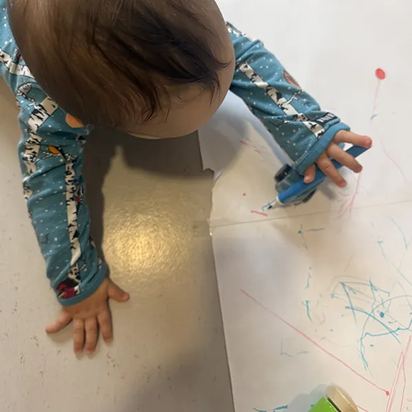 Un enfant à la crèche La Nanosphère à Lausanne dessine avec une voiture équipée d’un feutre sur une grande feuille au sol.