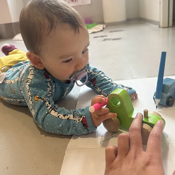 Un enfant à la crèche La Nanosphère à Lausanne dessine avec une voiture équipée d’un feutre sur une grande feuille au sol.